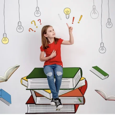 Une enfant assise sur une pile de livres, levant le doigt vers une ampoule